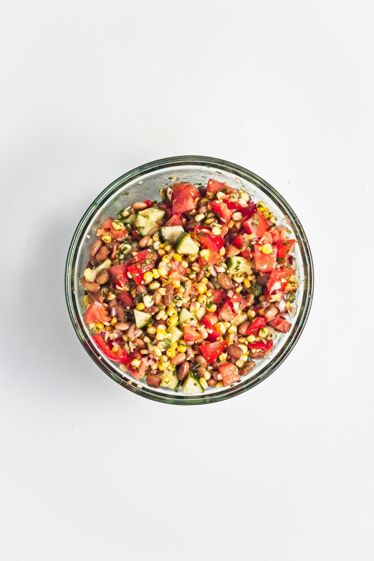 Mixed corn and pinto bean salad tossed with dressing in a glass bowl.