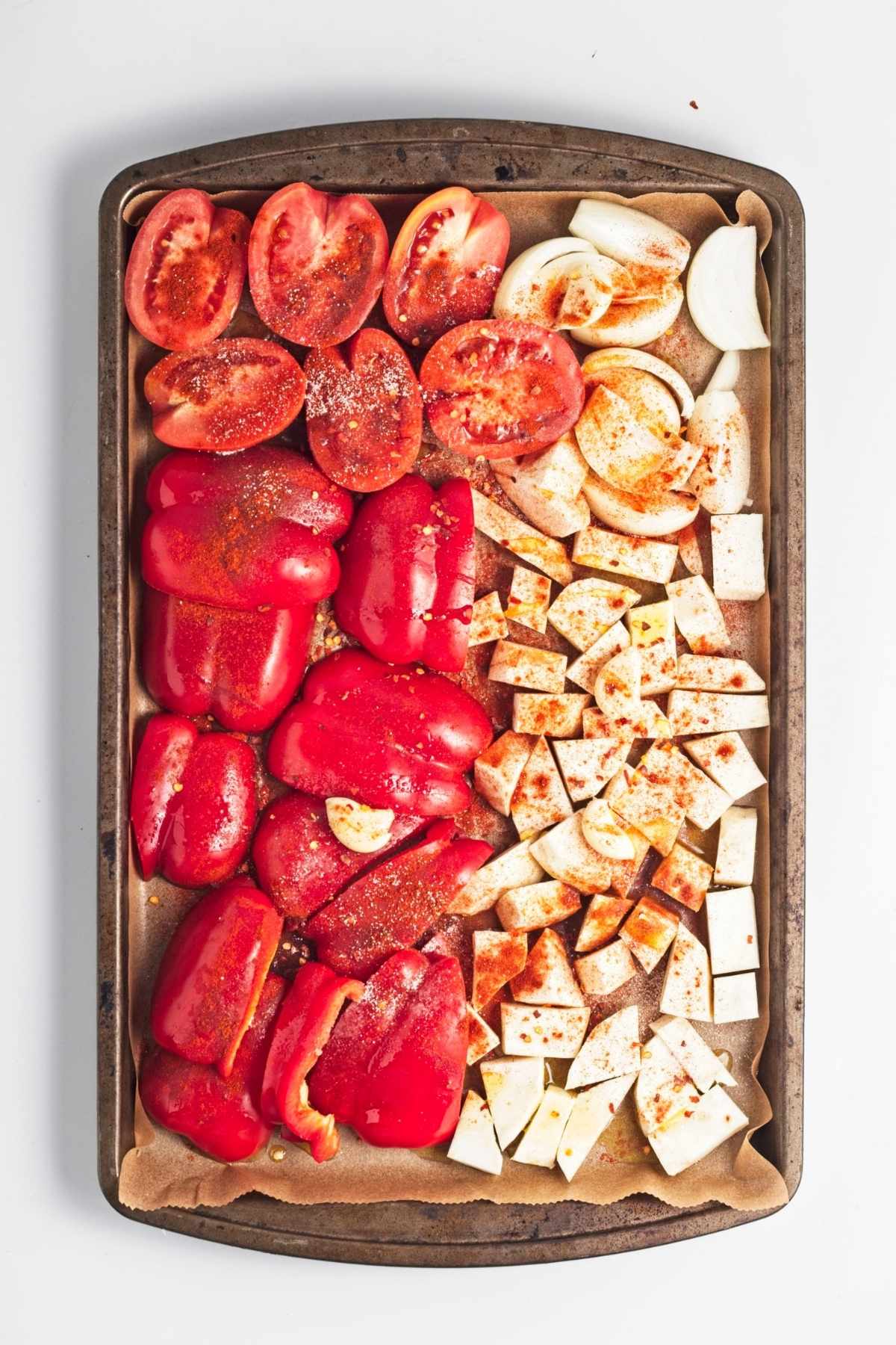 Chopped vegetables arranged on a lined baking tray, sprinkled with spices and olive oil.