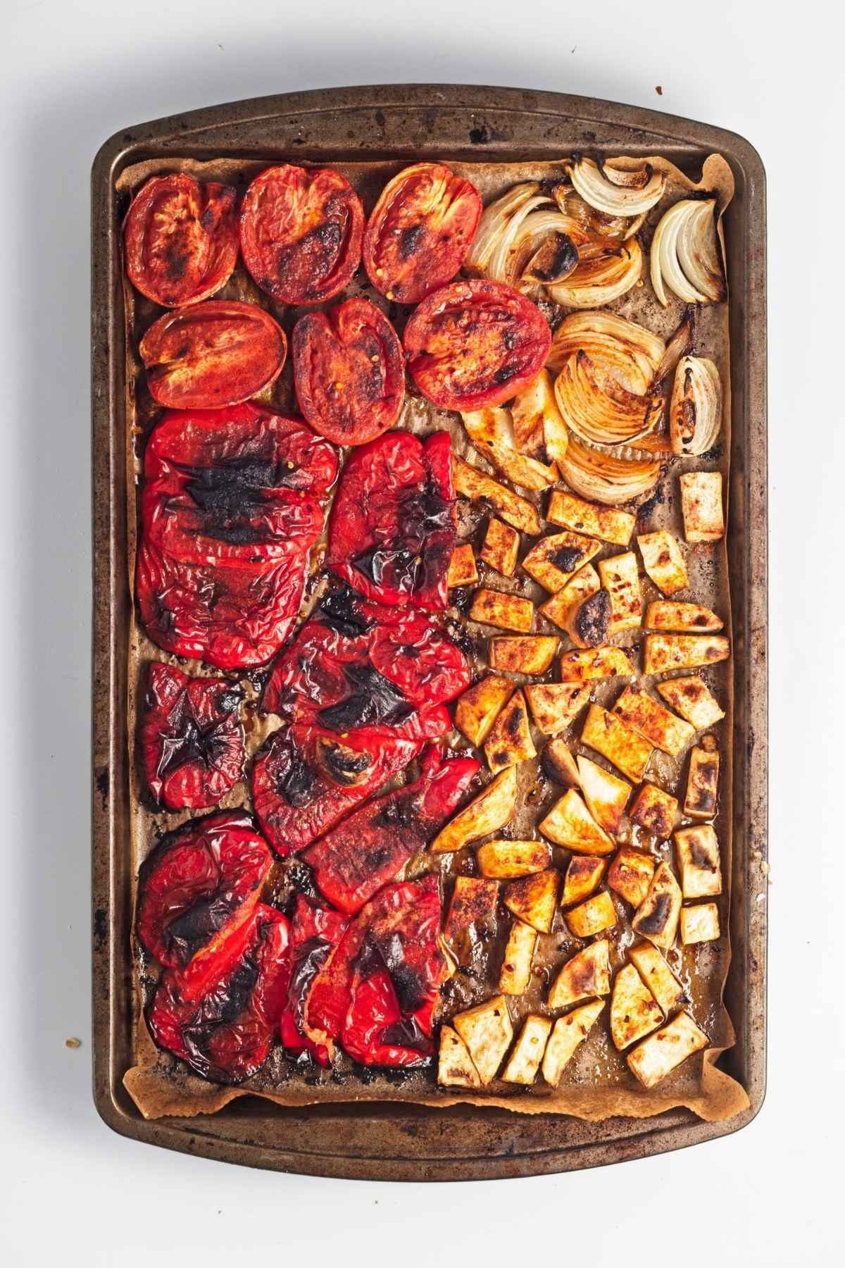 Roasted peppers, tomatoes, onion, garlic, and celeriac caramelizing on a baking tray.