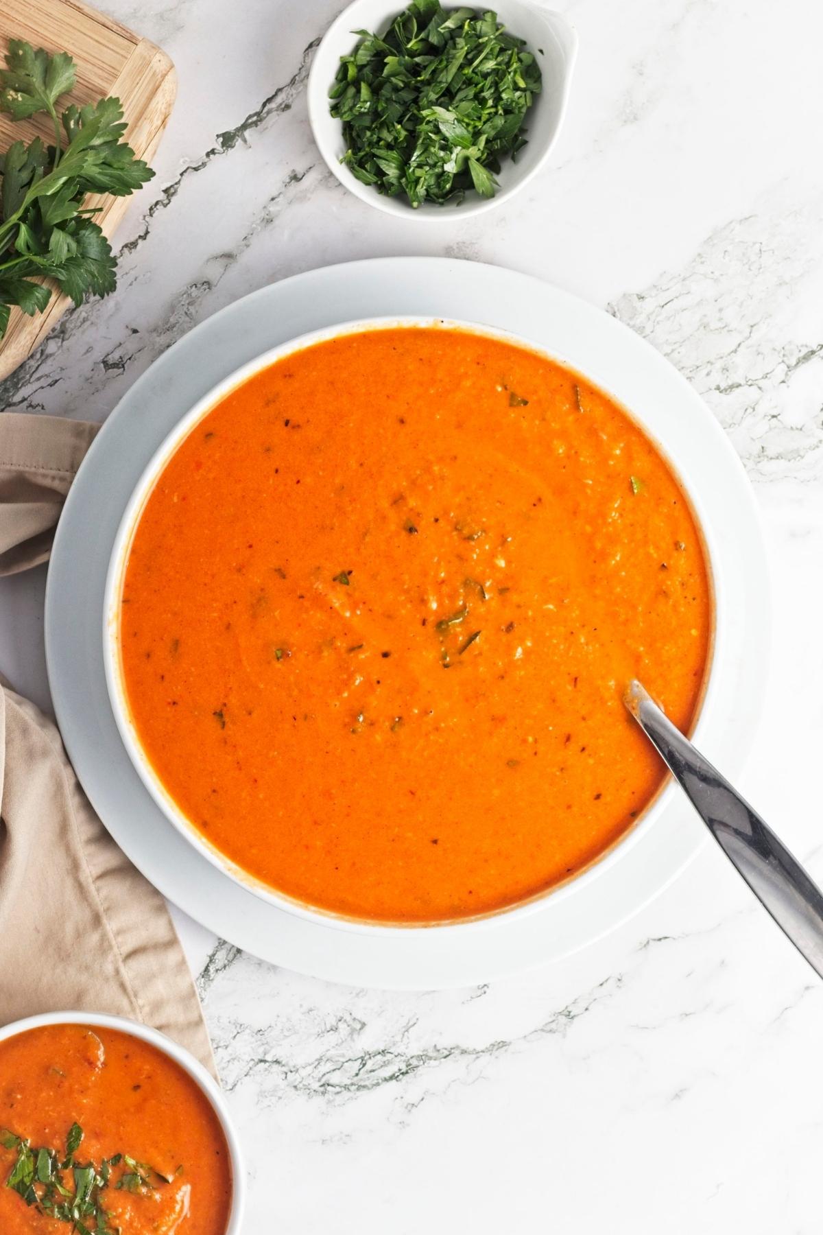 Smooth roasted red pepper soup poured into a pot and stirred with a spoon.
