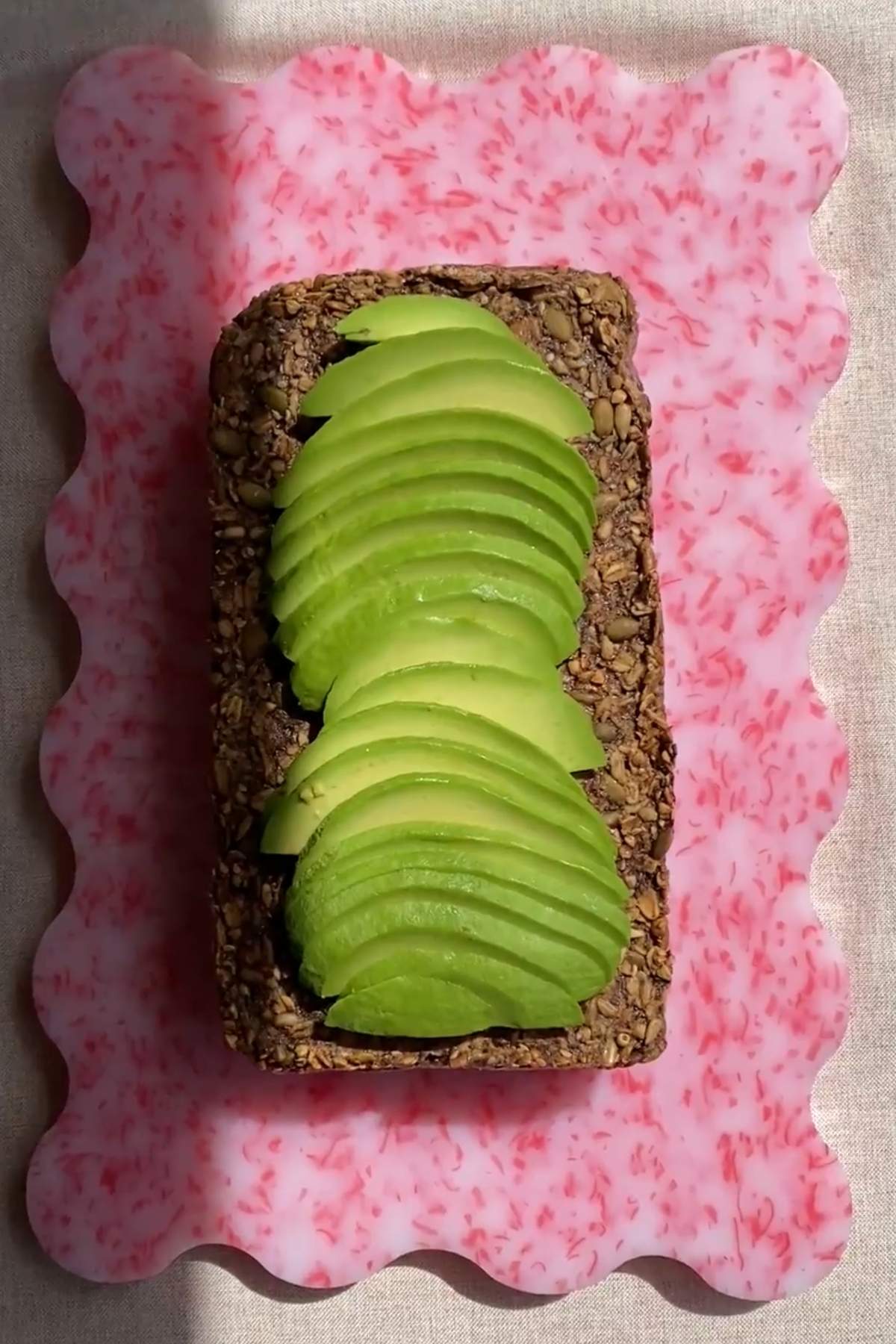Sliced avocado arranged on a piece of seeded bread on a pink plate.