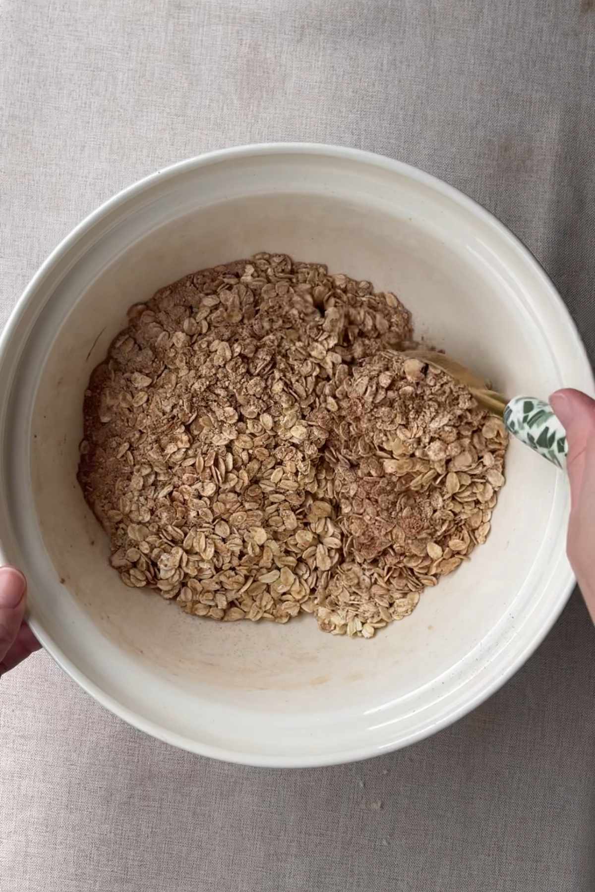 Dry rolled oats and cocoa being stirred together in a white mixing bowl.