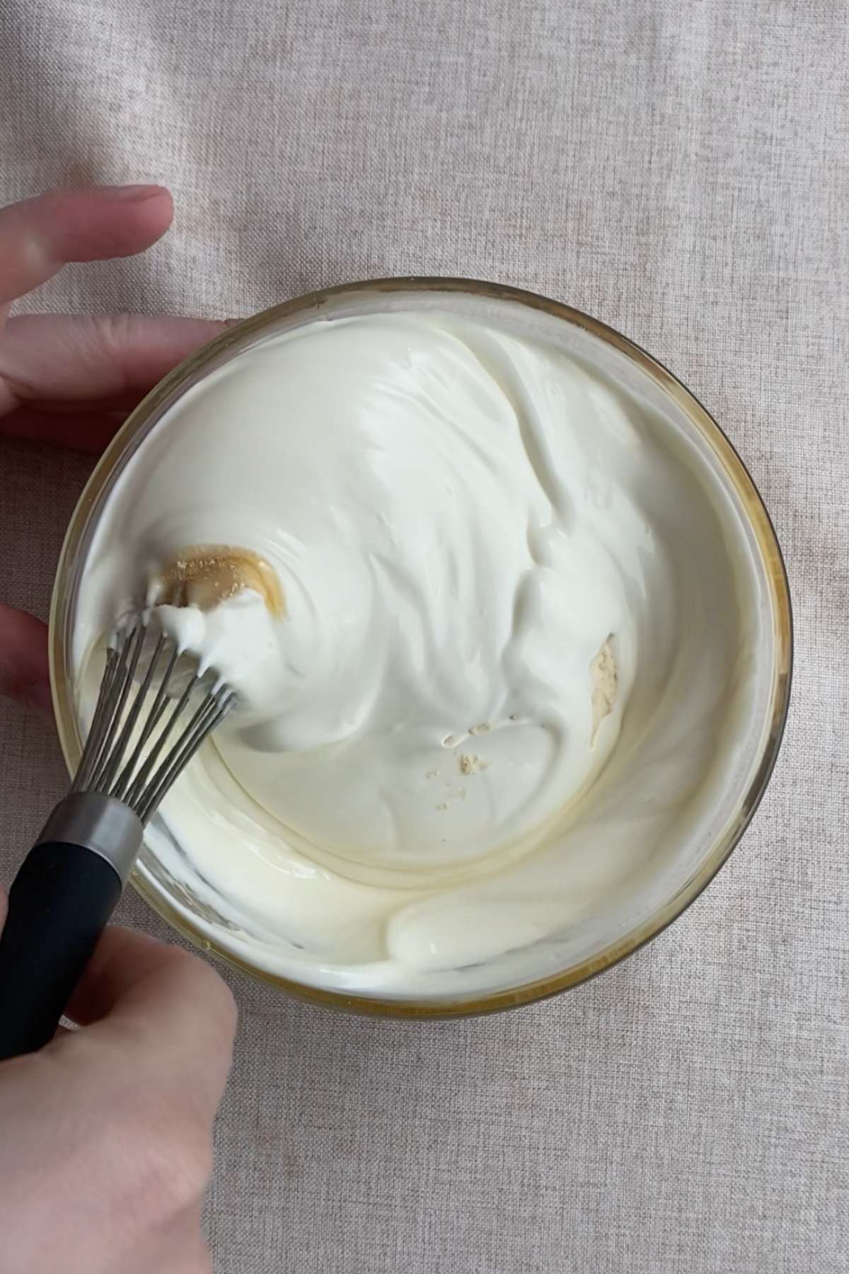 Whisking a thick yogurt mixture in a glass bowl until smooth.