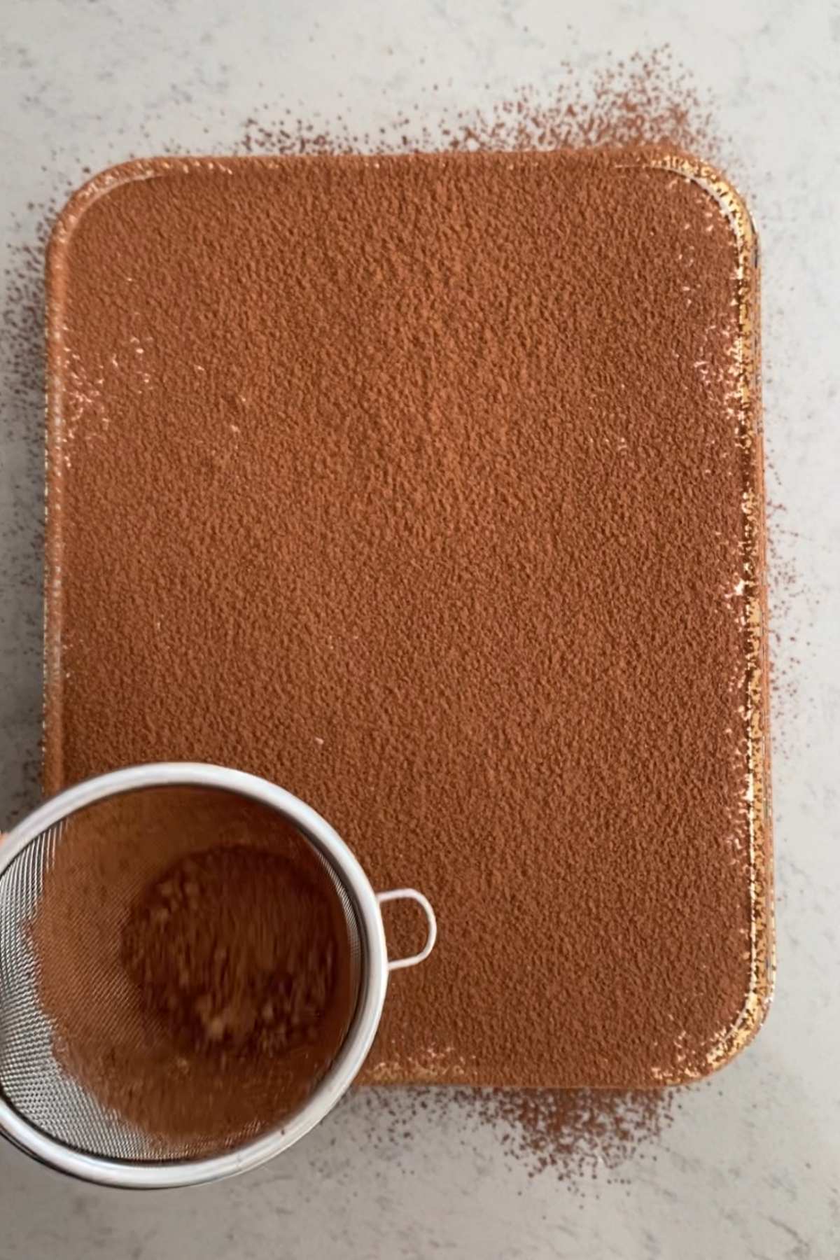 Dusting a tray of baked oats with a fine layer of cocoa powder using a mesh sieve.