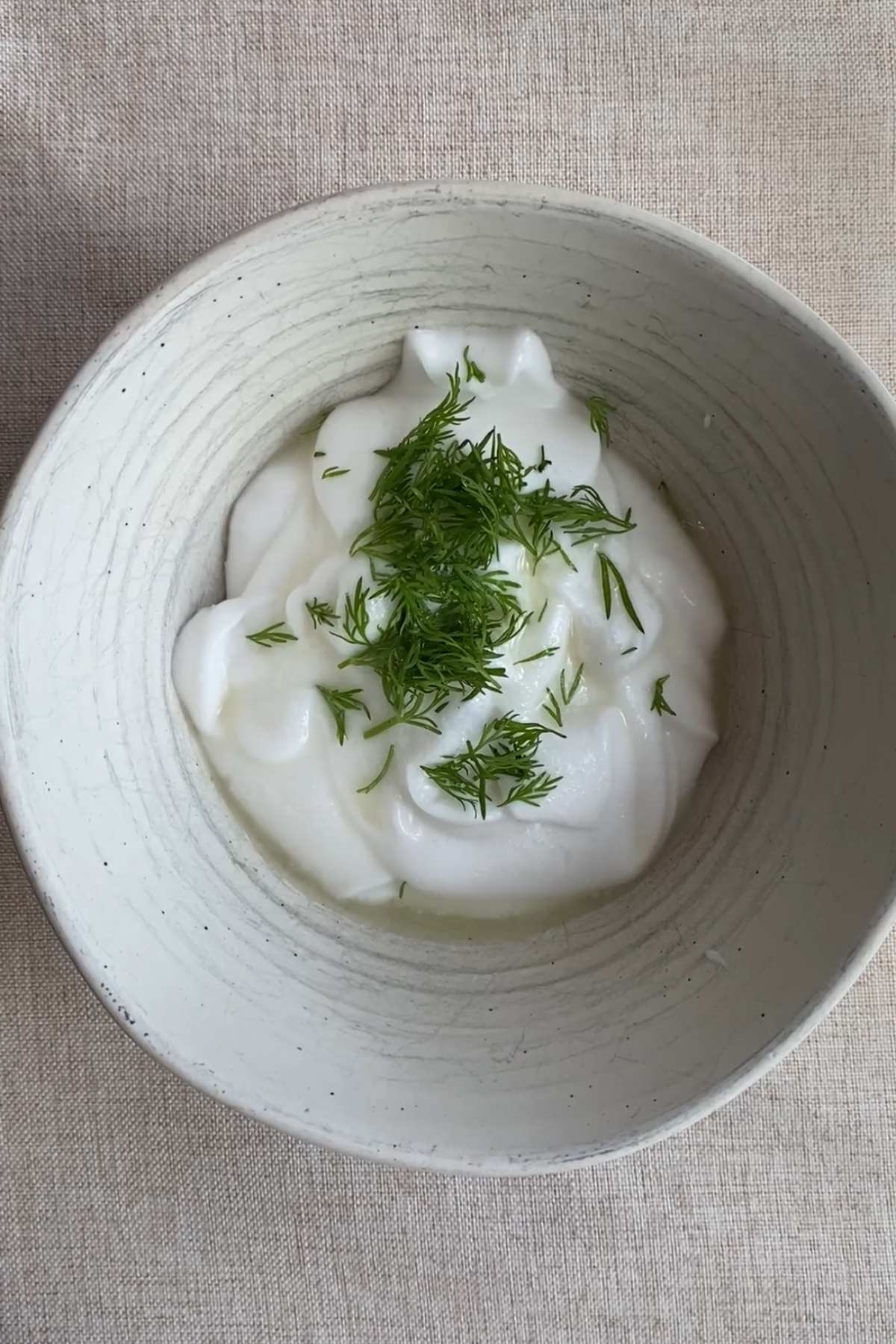 Creamy vegan yogurt sauce topped with fresh chopped dill in a ceramic bowl.