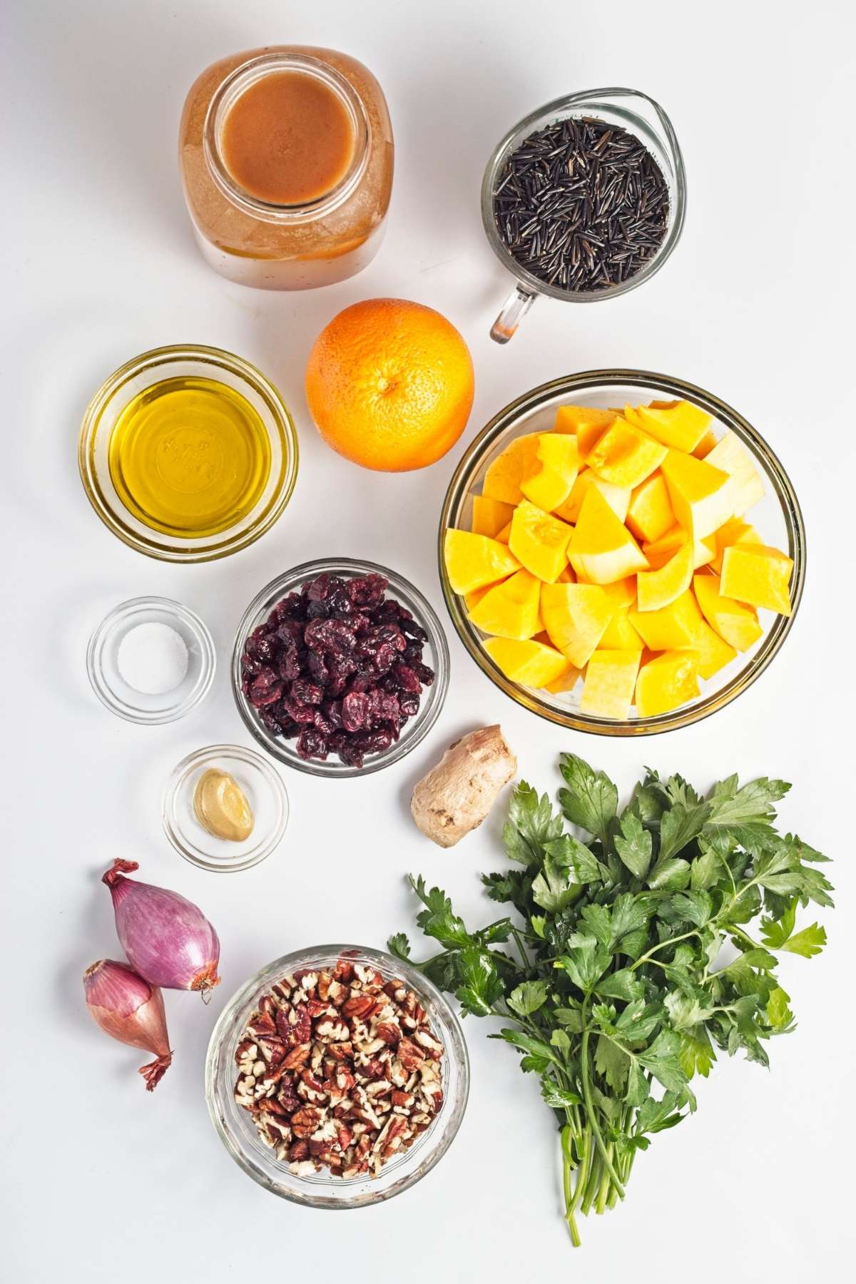Overhead view of wild rice, cubed butternut squash, orange, cranberries, pecans, parsley, ginger, shallots, oil, and dressing ingredients.