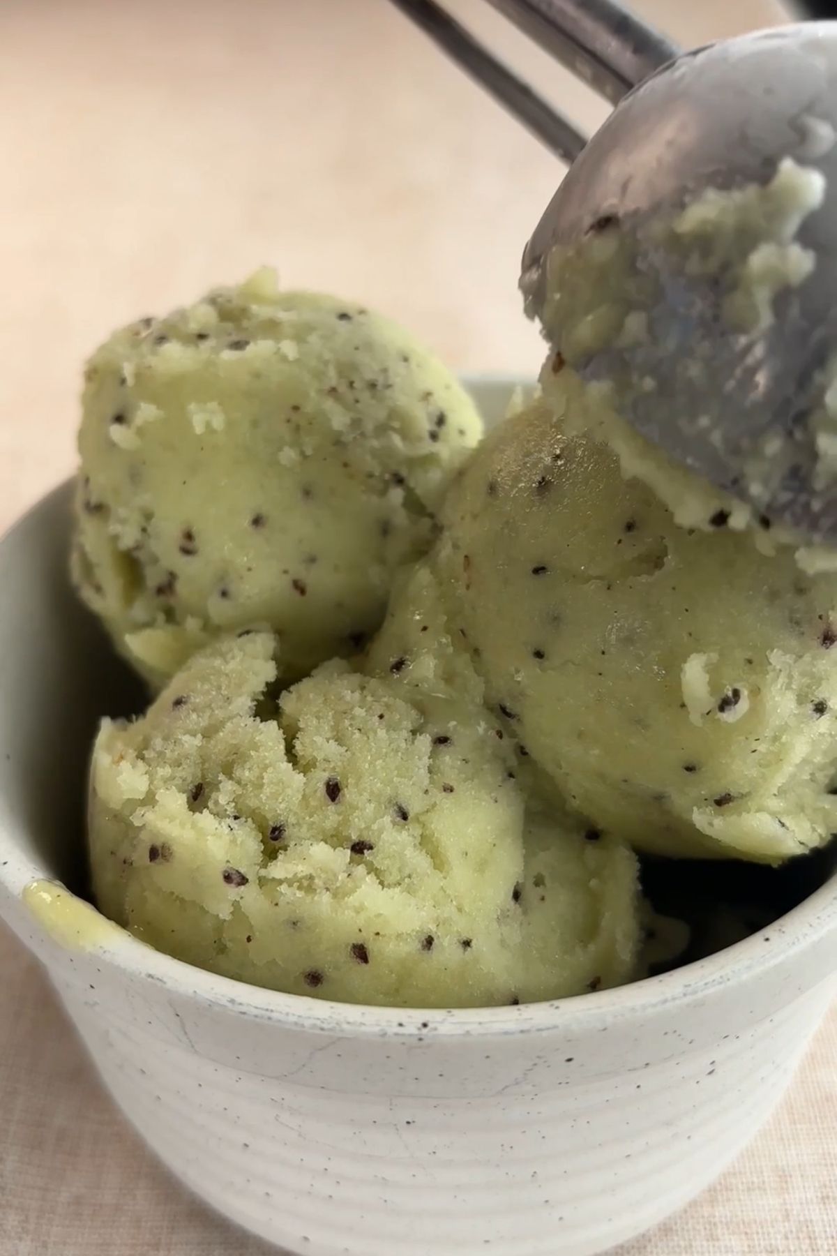 Spoon lifting a scoop of kiwi sorbet from a bowl, showing a soft, creamy texture with seeds.