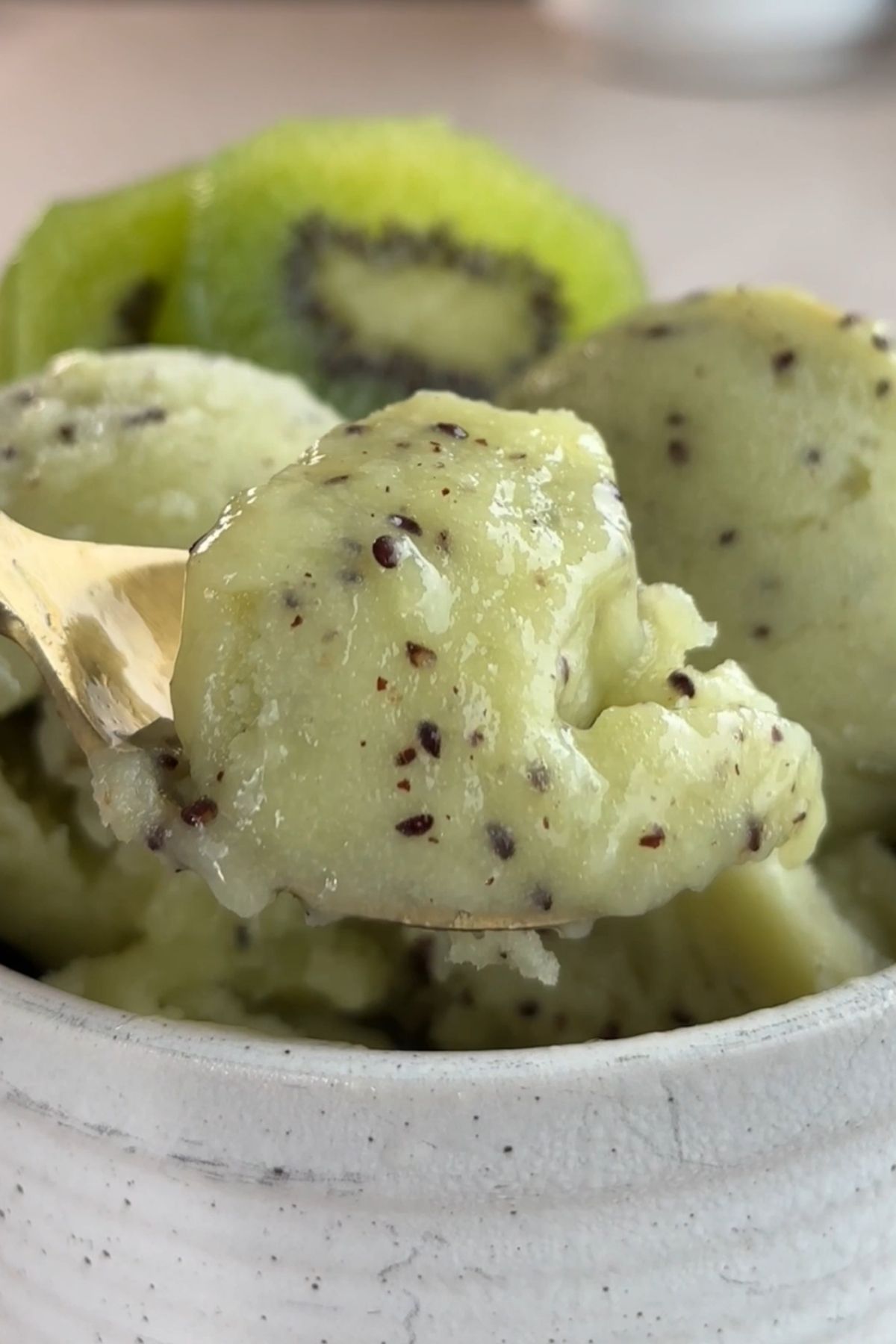 Close-up of kiwi sorbet scoops in a white bowl showing a smooth, icy texture with kiwi seeds.