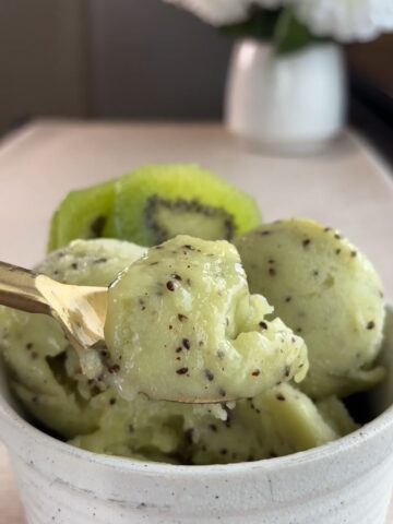 Kiwi sorbet scooped into a white bowl with visible kiwi seeds and sliced fresh kiwi behind.