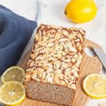 Gluten free lemon almond loaf topped with sliced almonds on a wooden board.
