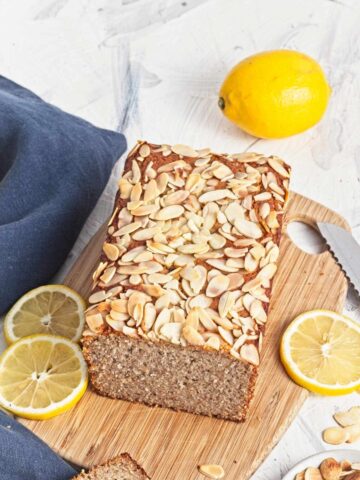 Gluten free lemon almond loaf topped with sliced almonds on a wooden board.