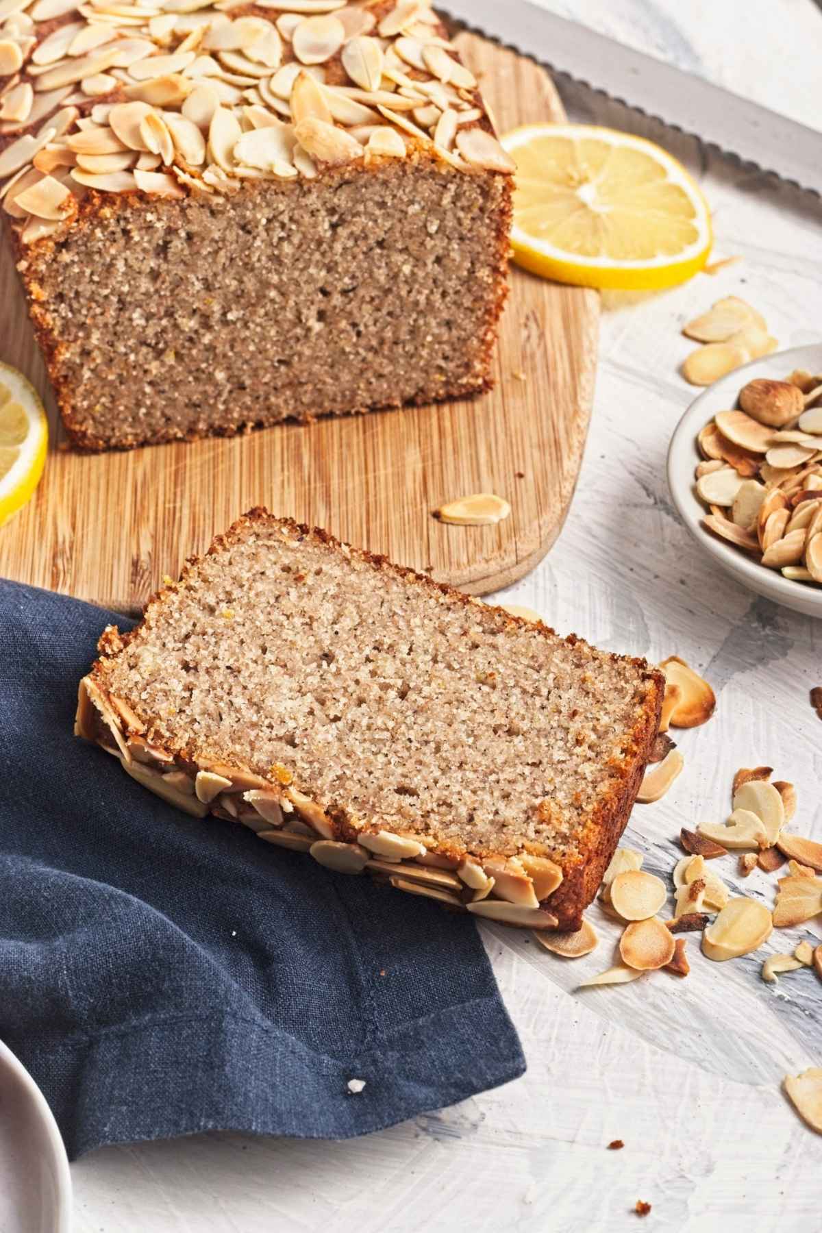 Single slice of lemon almond loaf served on a board with fresh lemon slices.