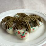 Matcha wreath cookies dipped in white chocolate with red and green sprinkles on a plate.