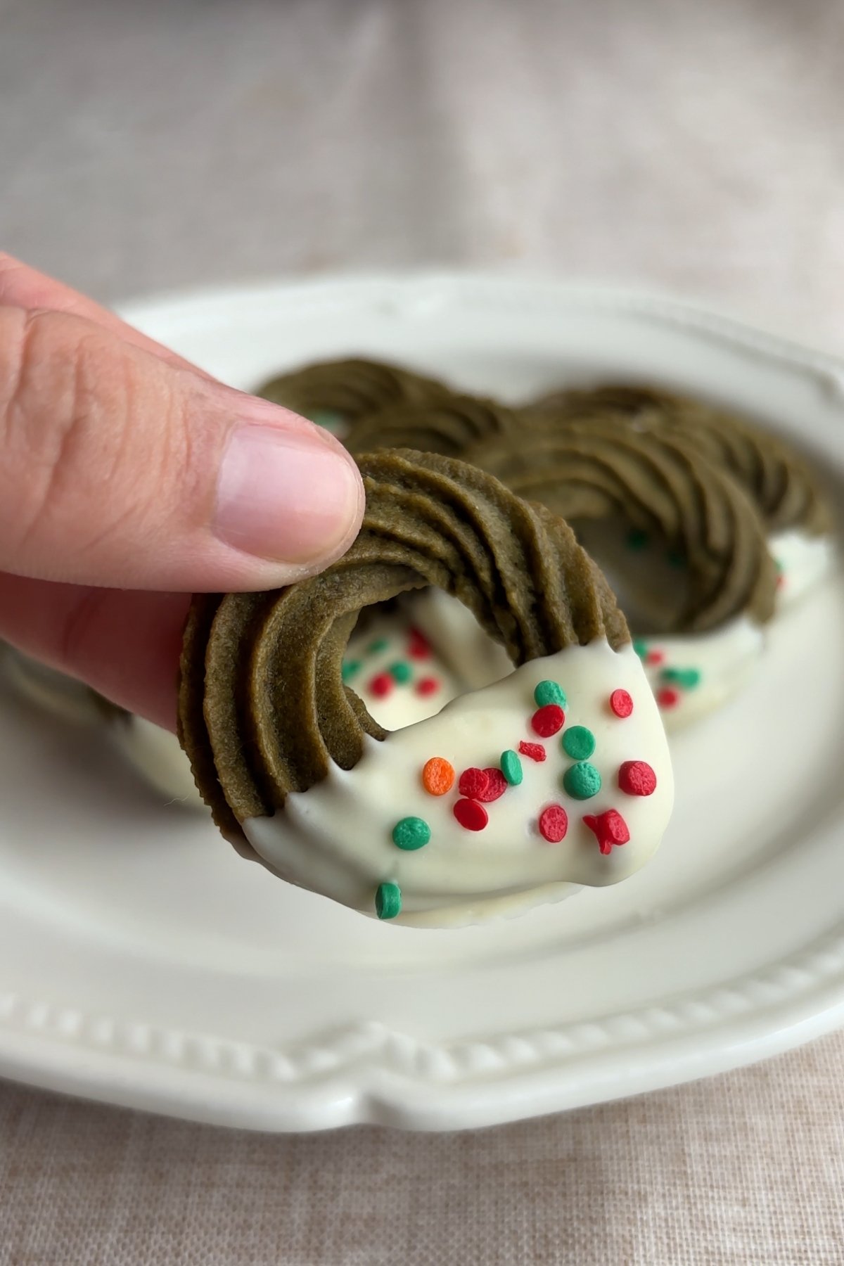 Hand holding up matcha wreath cookie with white chocolate coating and festive sprinkles.