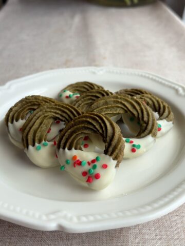Matcha wreath cookies dipped in white chocolate with red and green sprinkles on a plate.