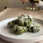 Stack of matcha crinkle cookies on a white plate, thick cracks and powdered sugar coating visible.