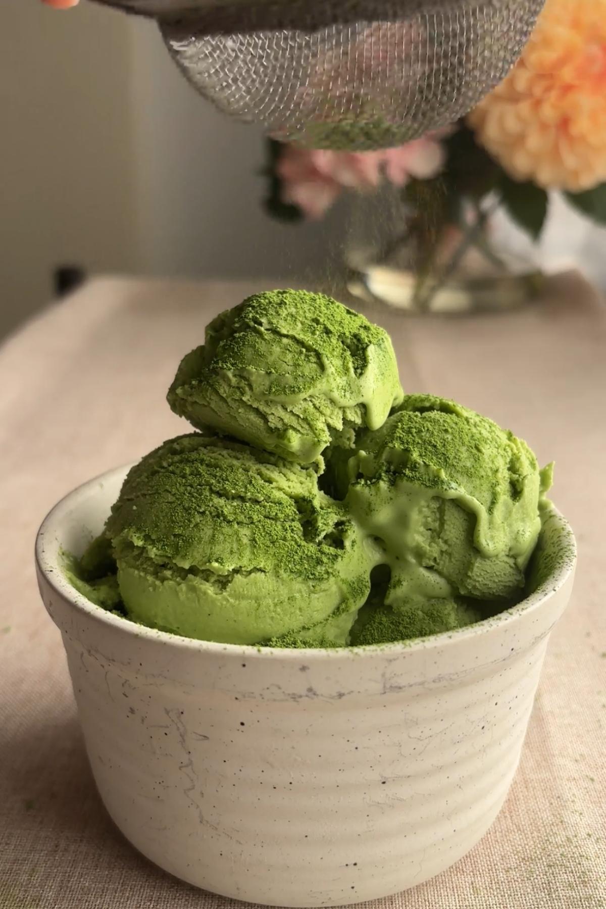 Fine green powder being sifted over scoops of green ice cream.