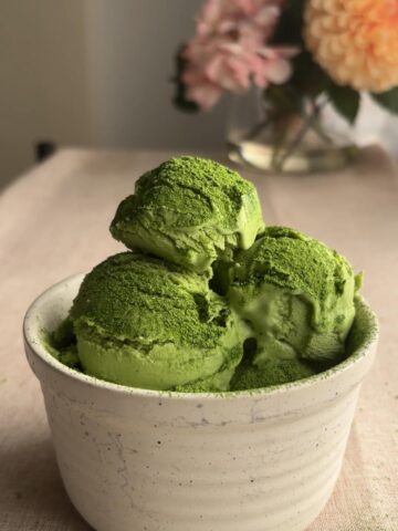 Three scoops of green ice cream stacked in a ceramic bowl.