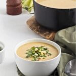 Creamy corn soup served in a white bowl, topped with herbs and corn.