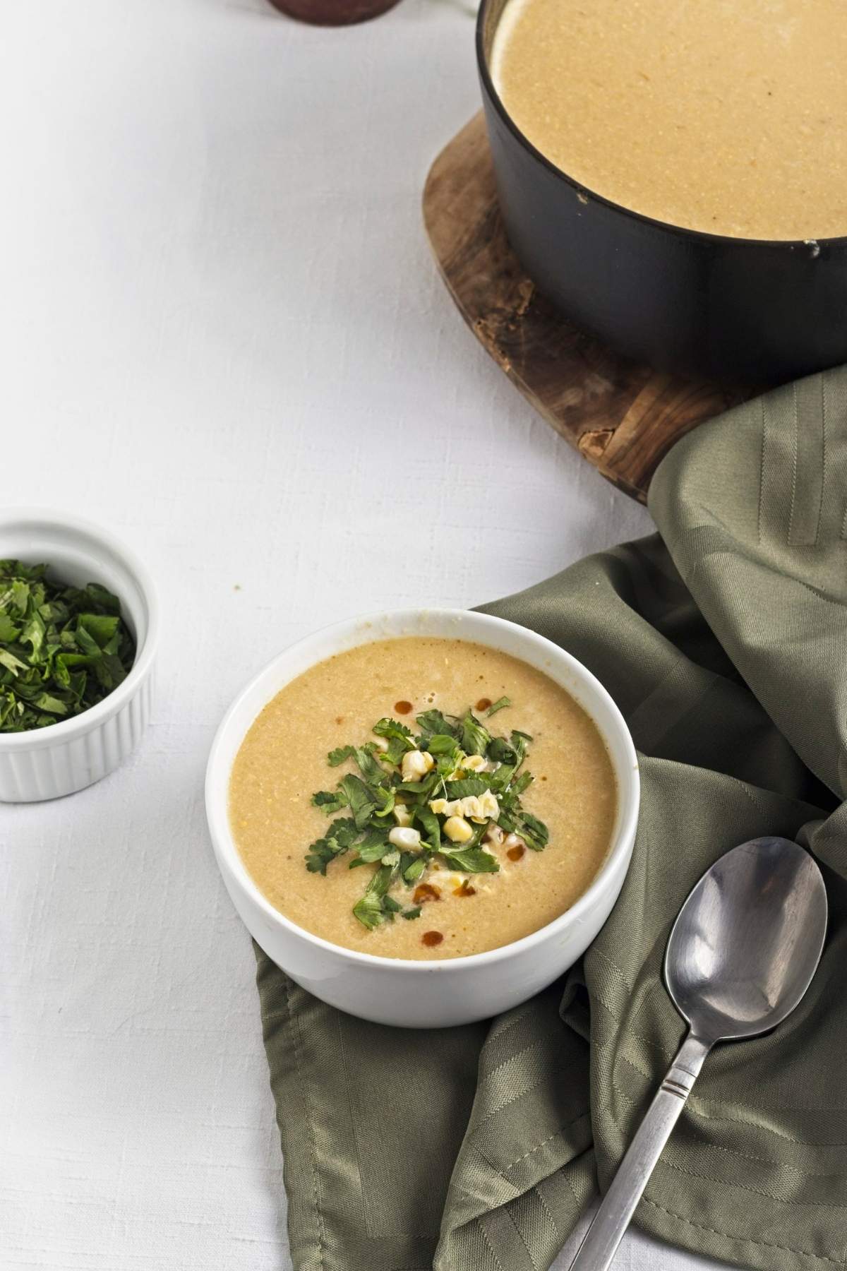 Corn soup served beside a pot, styled with a spoon and folded cloth.