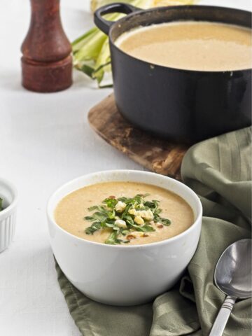 Creamy corn soup served in a white bowl, topped with herbs and corn.