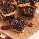 Pecan bars arranged on wooden board with visible layers of crust and sticky pecan topping.