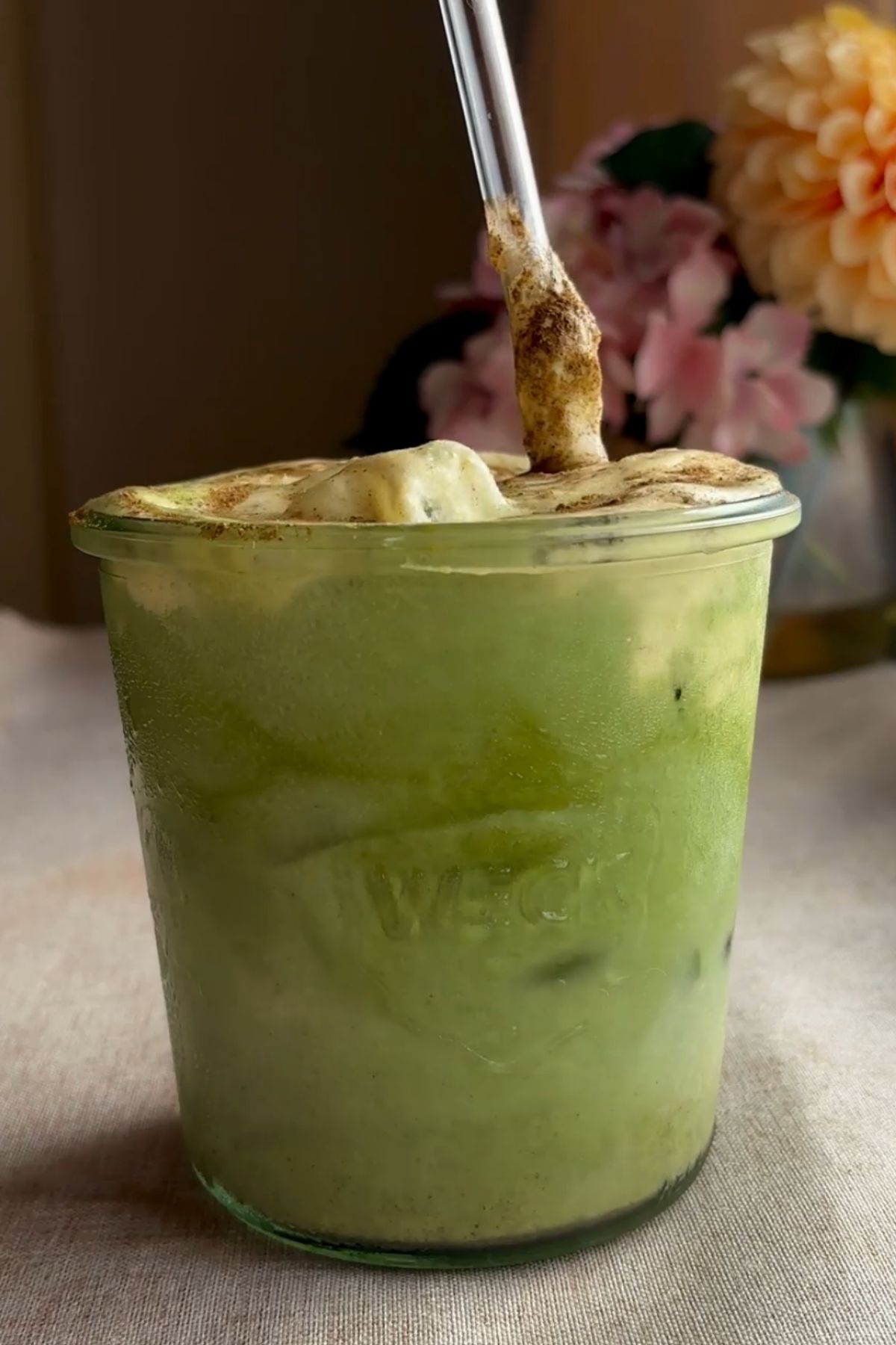Glass jar of iced matcha latte showing swirls of matcha and spiced milk.