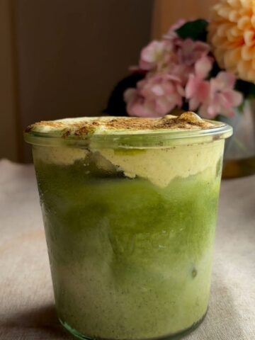Iced matcha latte with pumpkin cold foam in a glass jar, dusted with pumpkin spice.