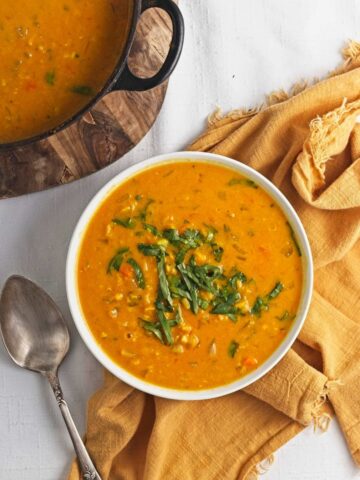 Creamy orange lentil soup served in a white bowl with chopped herbs on top.
