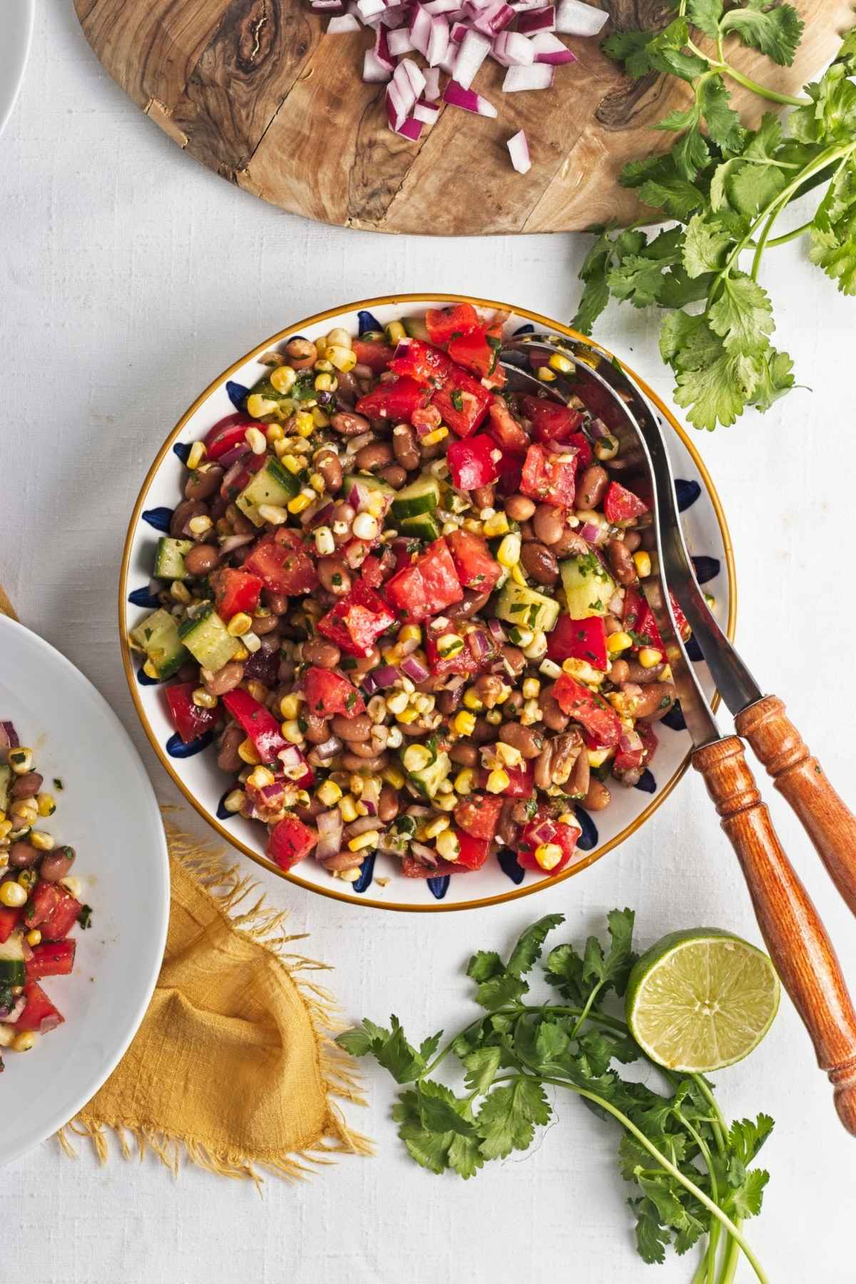 Pinto bean and roasted corn salad served on a white plate with cucumber, tomato, and lime on the side.