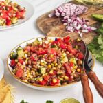 Roasted corn and pinto bean salad with tomatoes, cucumber, red onion, and herbs in a patterned serving bowl.
