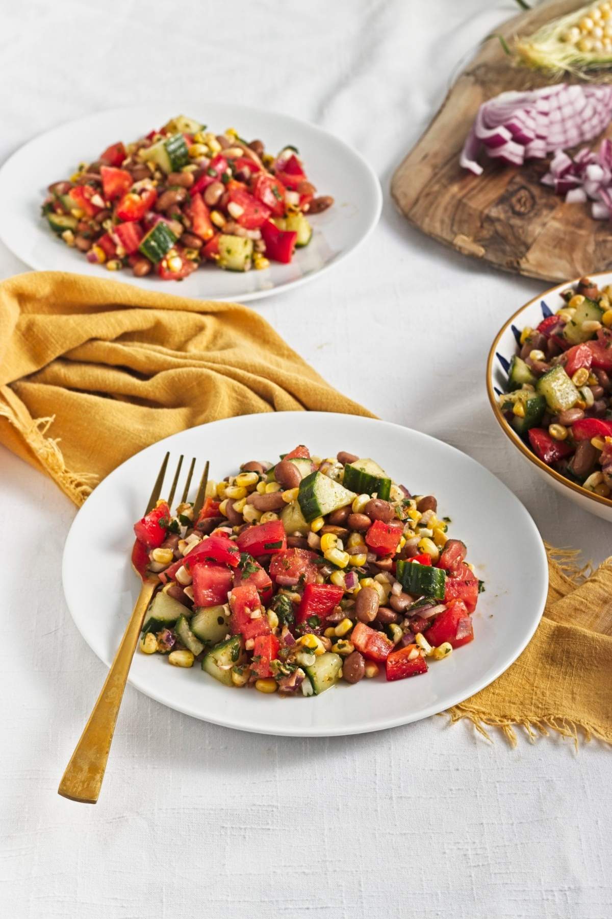 Large bowl of corn and pinto bean salad with chopped tomatoes, cucumber, red onion, and fresh herbs.