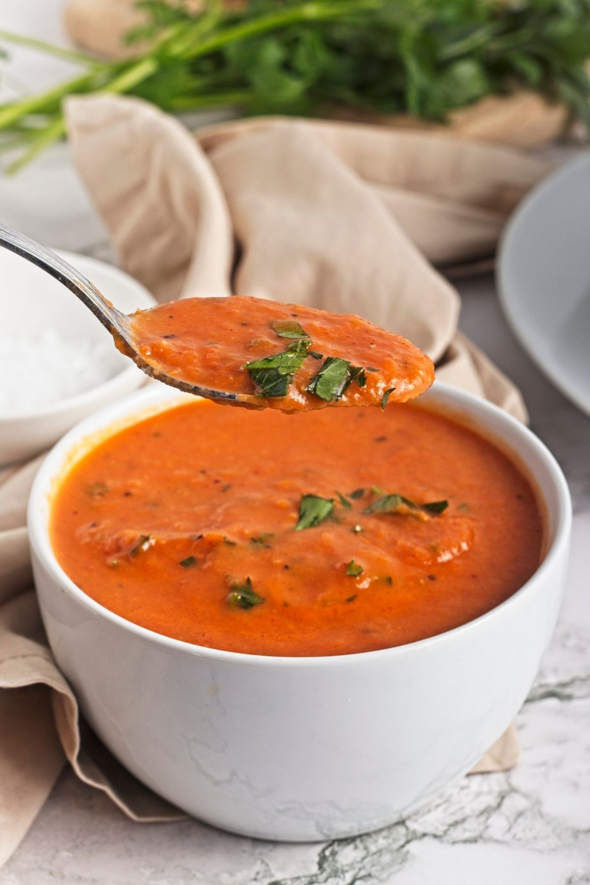 Spoon lifting creamy roasted red pepper soup from a white bowl.