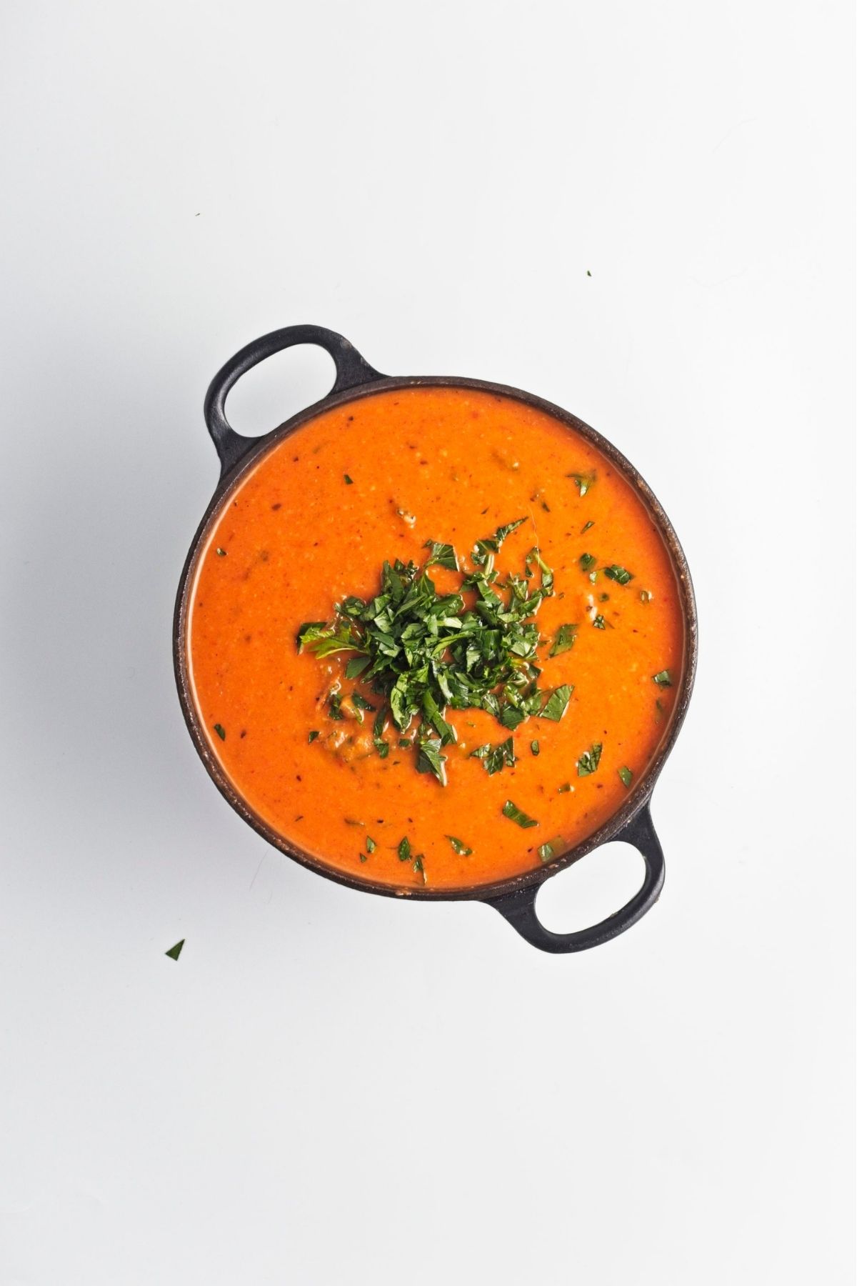 Top-down view of roasted red pepper soup garnished with chopped parsley.