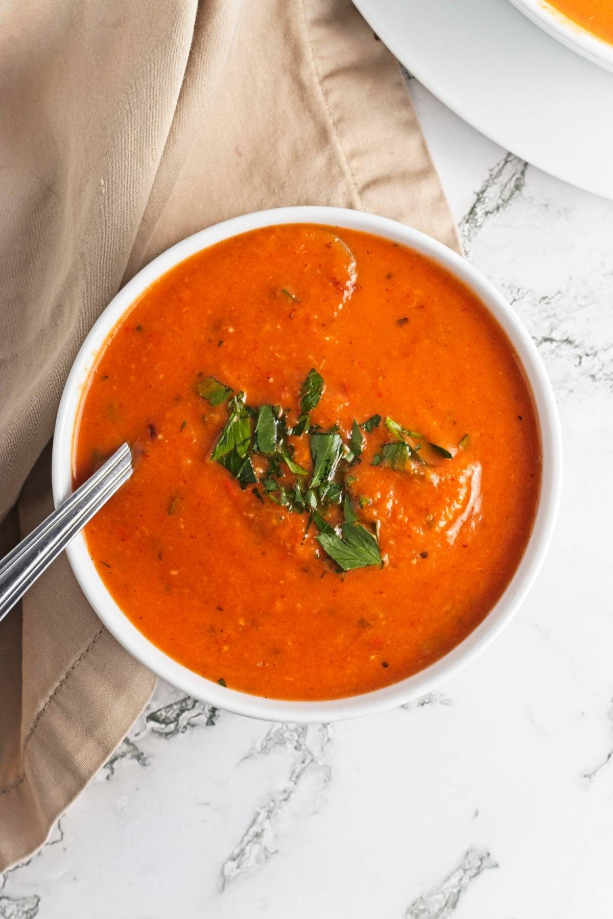 Creamy roasted red pepper soup served in a white bowl on a marble surface.