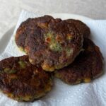 Golden zucchini chickpea fritters stacked on a paper towel-lined plate.