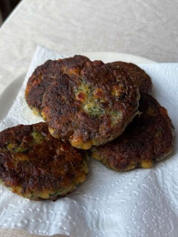 Golden zucchini chickpea fritters stacked on a paper towel-lined plate.