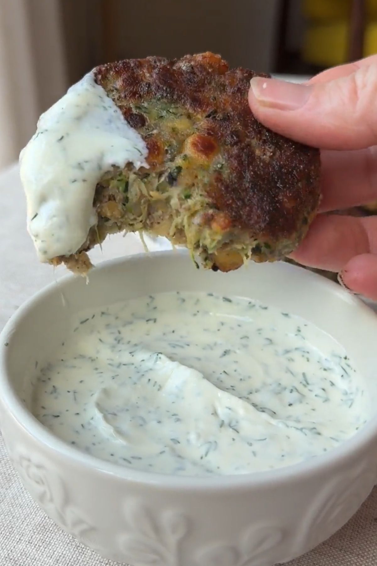 Zucchini chickpea fritter dipped into a bowl of creamy yogurt sauce.