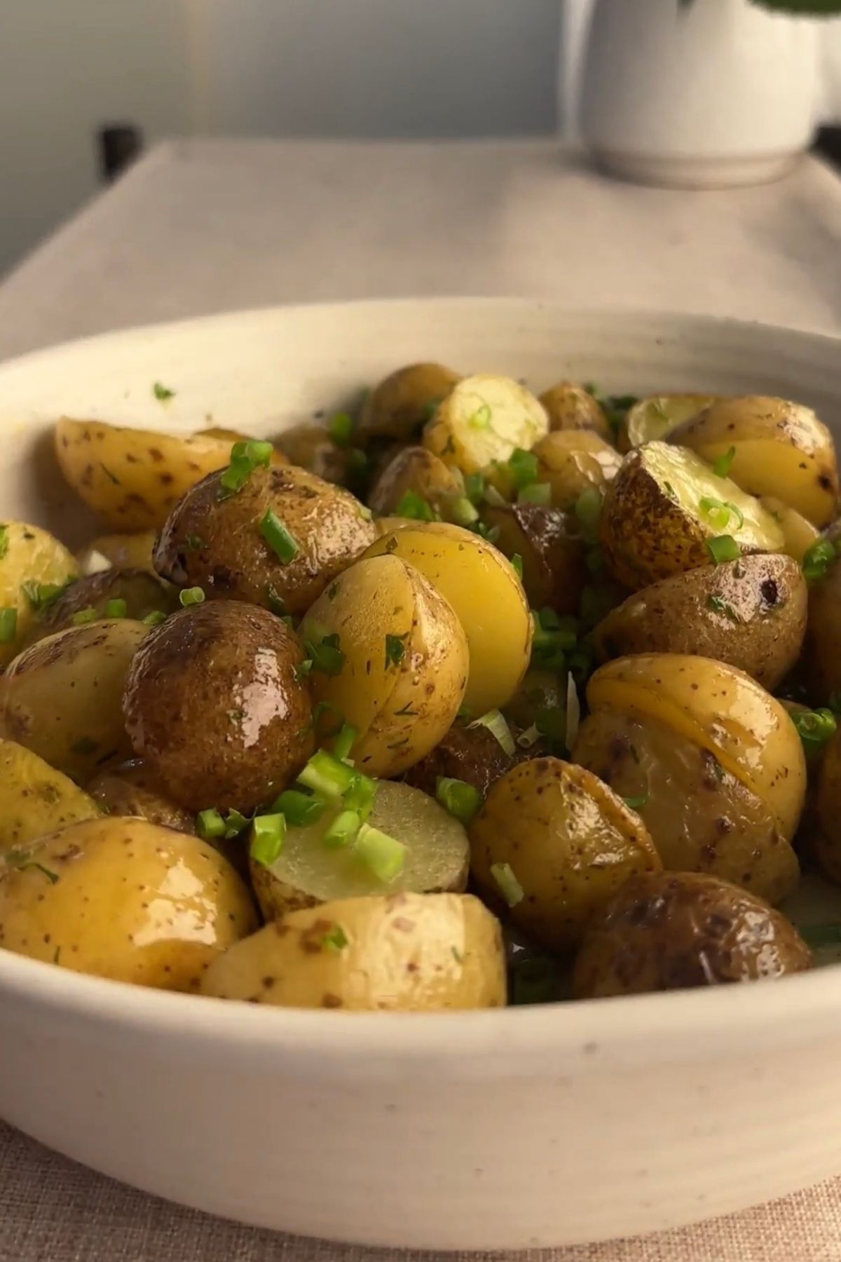 French potato salad made with halved baby potatoes tossed in a lemon Dijon vinaigrette with fresh herbs and capers, served in a white bowl.
