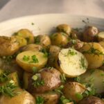 Close-up of French potato salad with glossy baby potatoes coated in lemon Dijon dressing and sprinkled with chopped herbs.