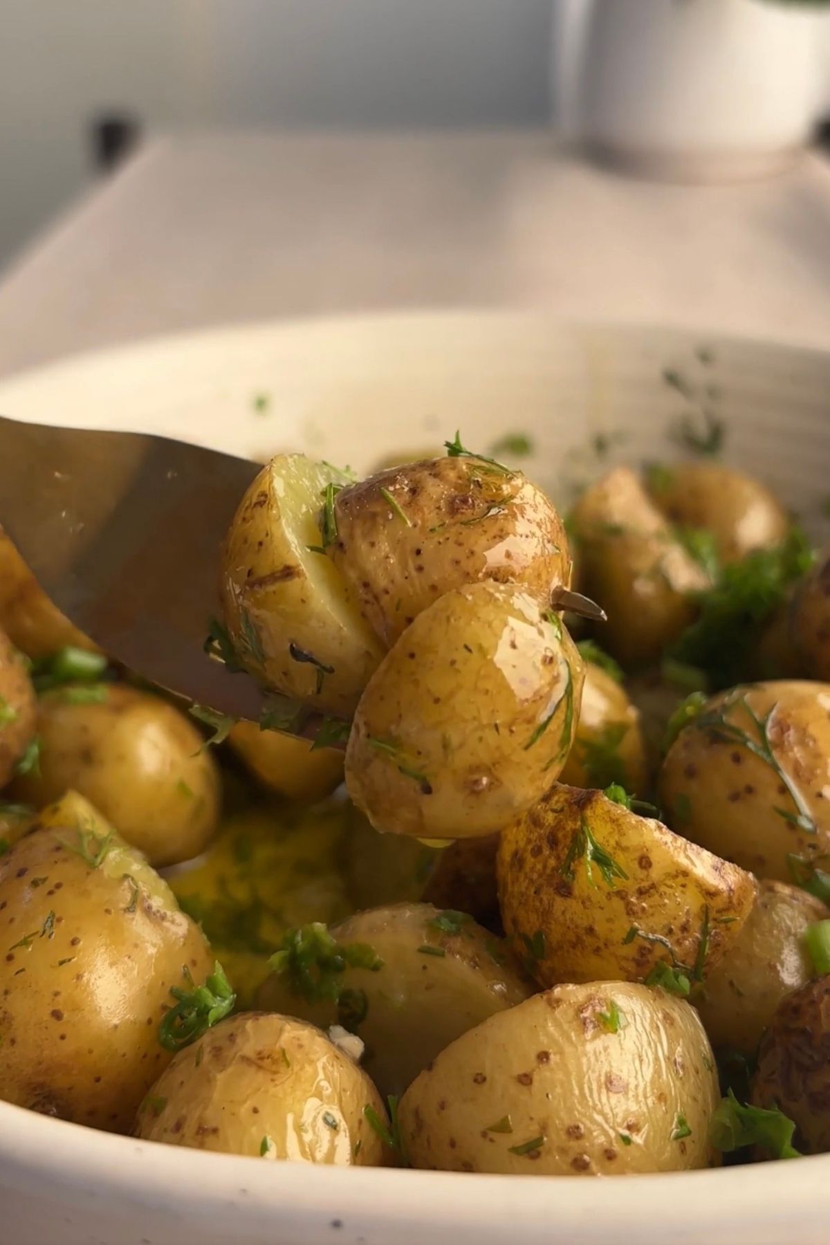 Fork lifting tender baby potatoes from a bowl of French potato salad dressed in lemon Dijon vinaigrette with herbs and capers.
