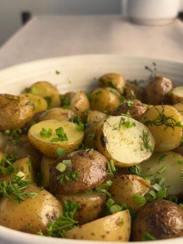 Close-up of French potato salad with glossy baby potatoes coated in lemon Dijon dressing and sprinkled with chopped herbs.