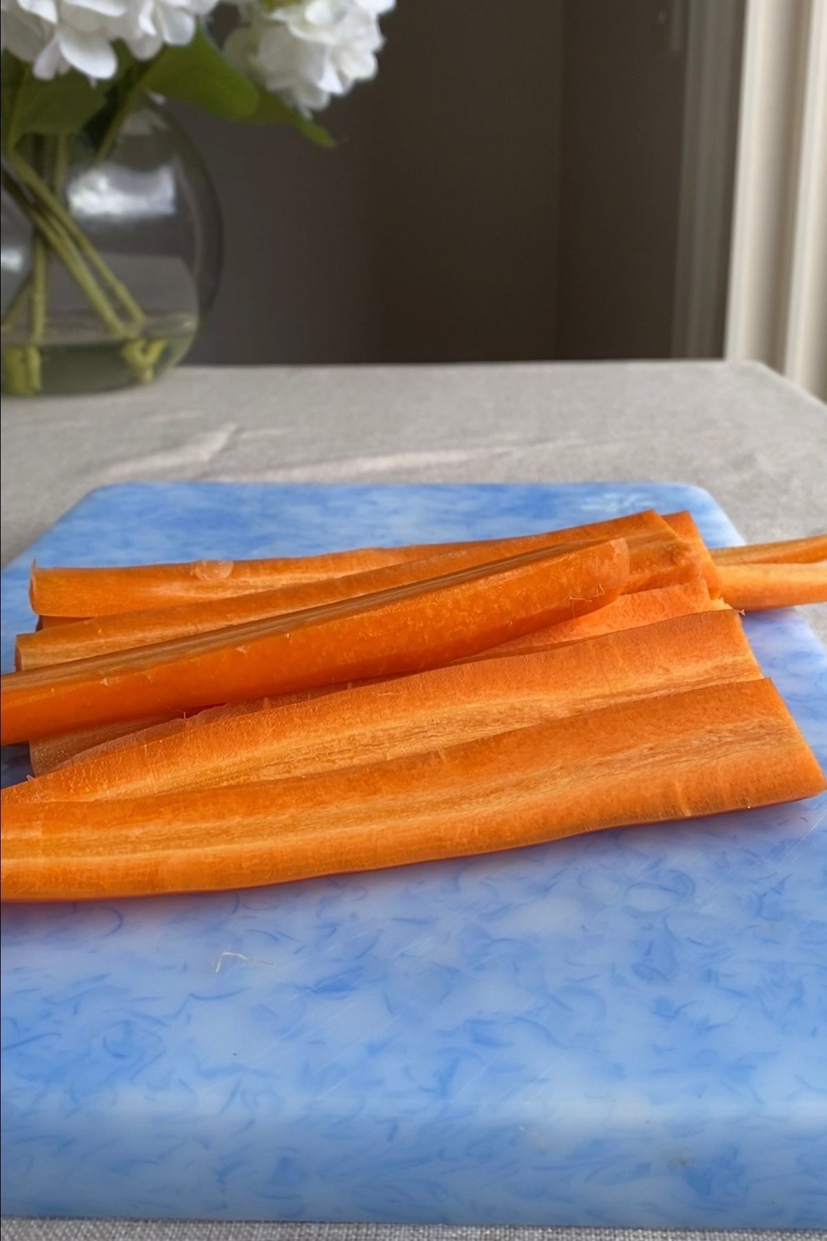 Peeled carrots sliced lengthwise on a blue cutting board, ready for roasting.