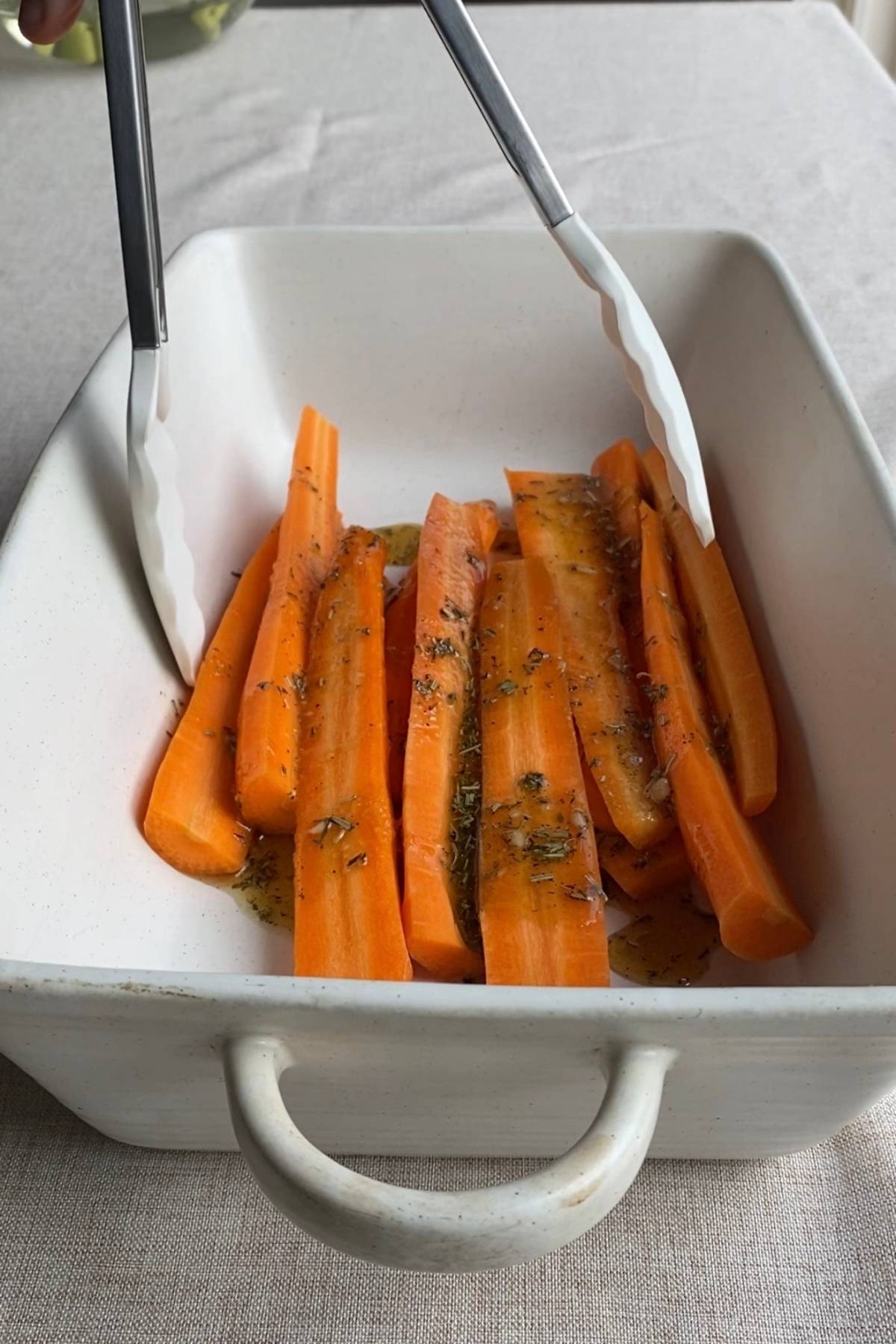 Carrots arranged in a baking dish with oil and dried herbs scattered over the top.