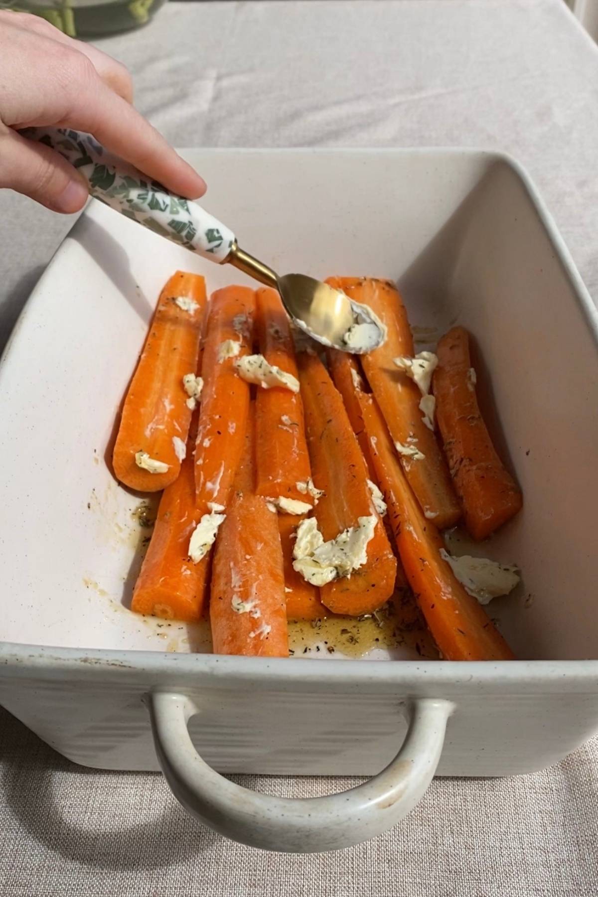 Vegan butter spooned over raw carrots in a roasting dish.