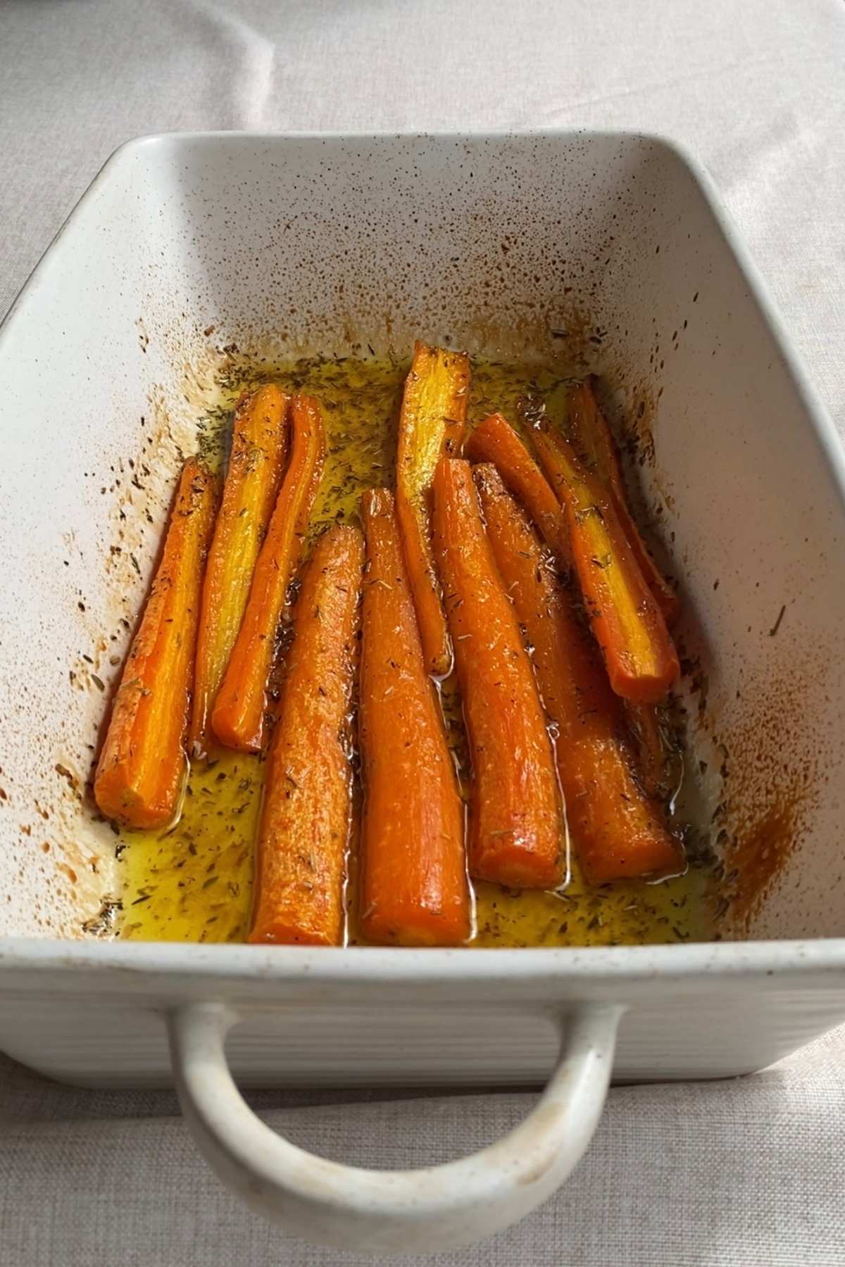 Roasted carrots resting in a baking dish with caramelized glaze and herbs.