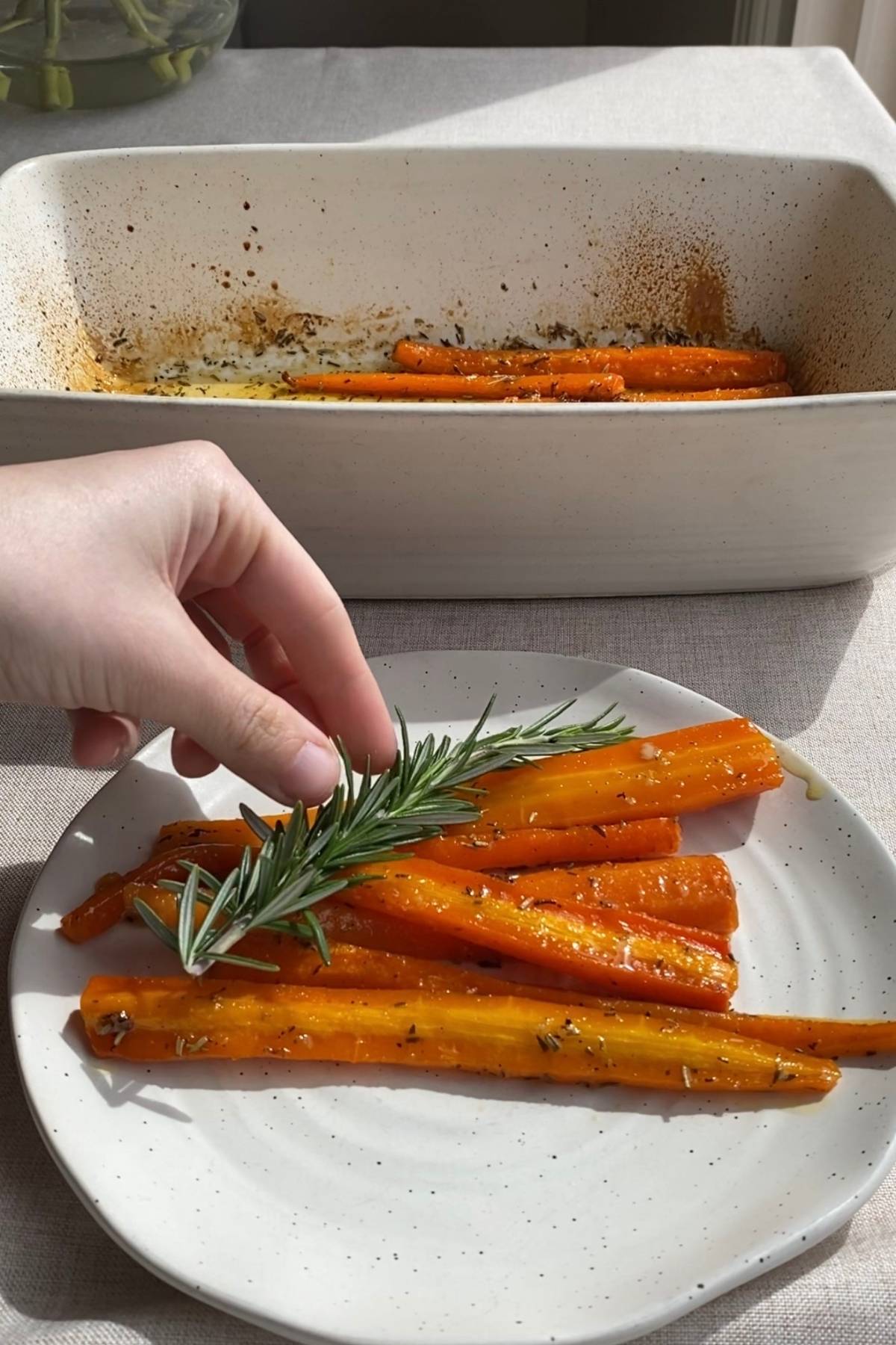 Glossy roasted carrots arranged on a plate and topped with a rosemary sprig.