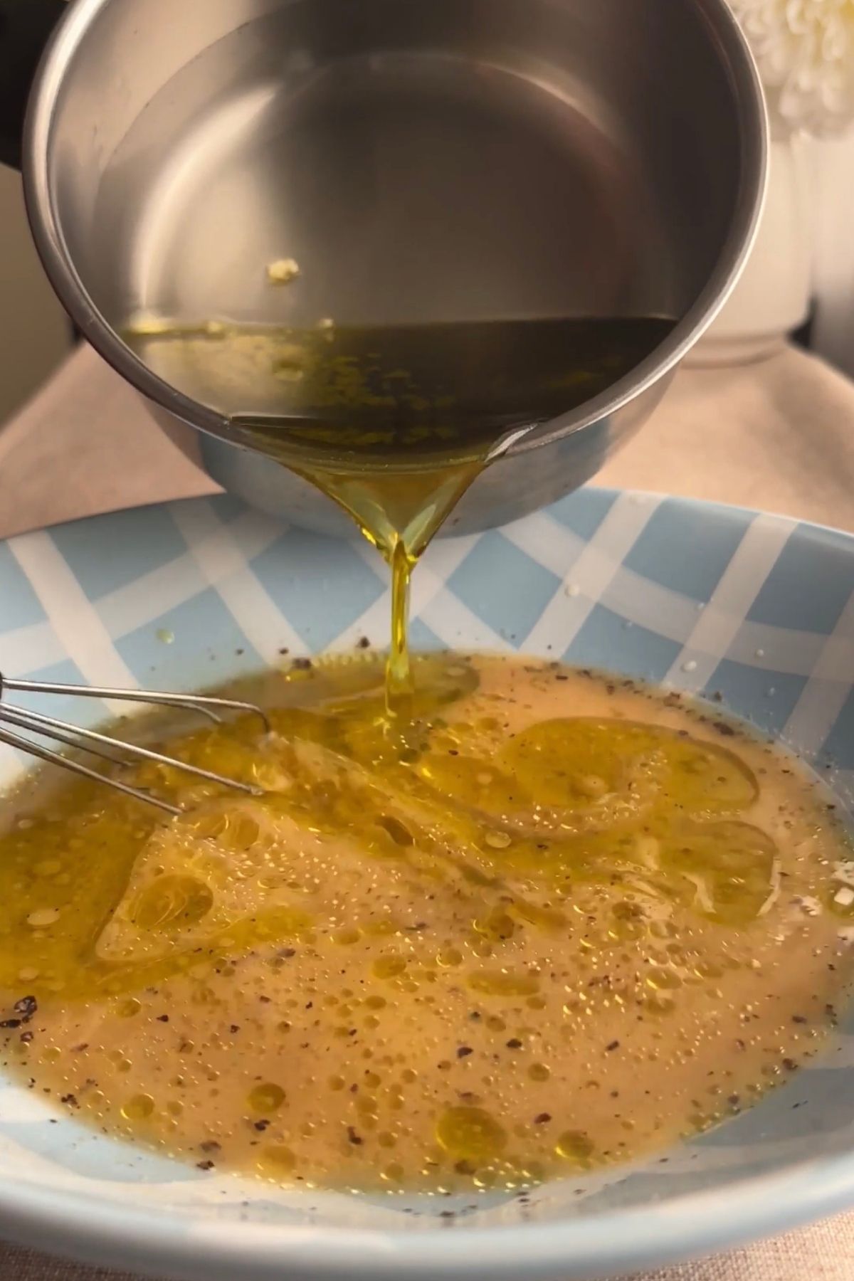 Warm olive oil being poured into a bowl with lemon juice and vinegar.
