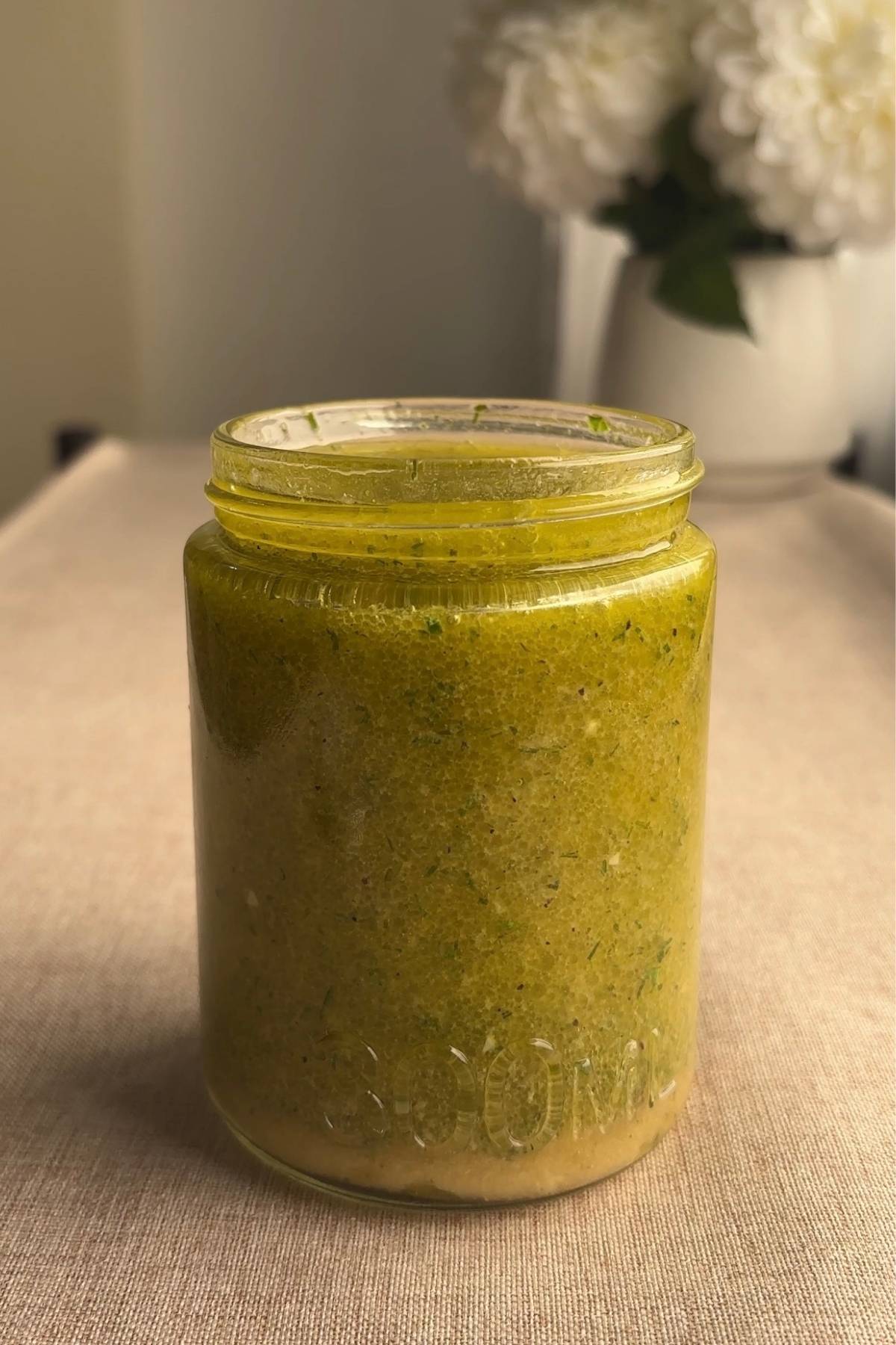 Finished lemon Dijon dressing with chopped herbs in a glass jar.