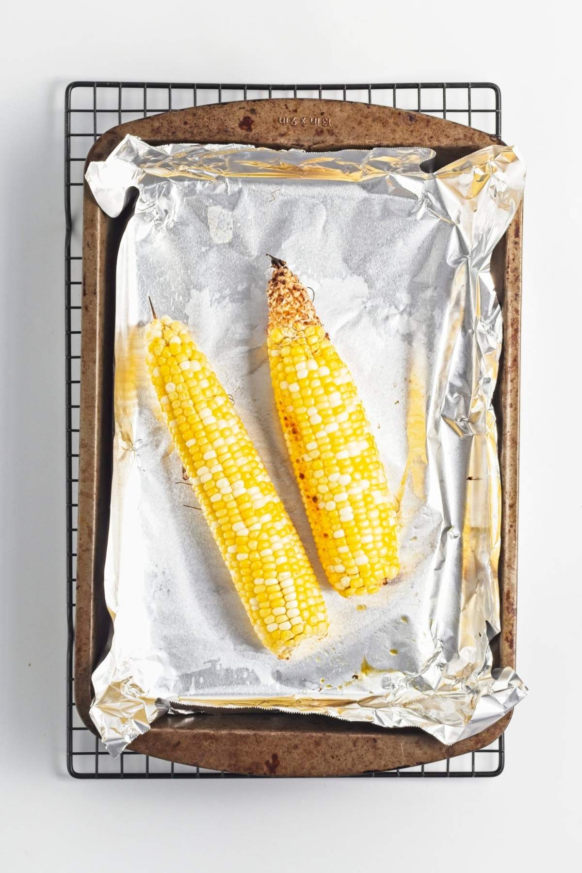 Roasted corn cobs cooling on a baking tray lined with foil.